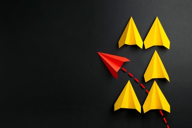 Image of Red paper plane with flight path turning other way, among yellow ones on black background. Dashed line for trajectory