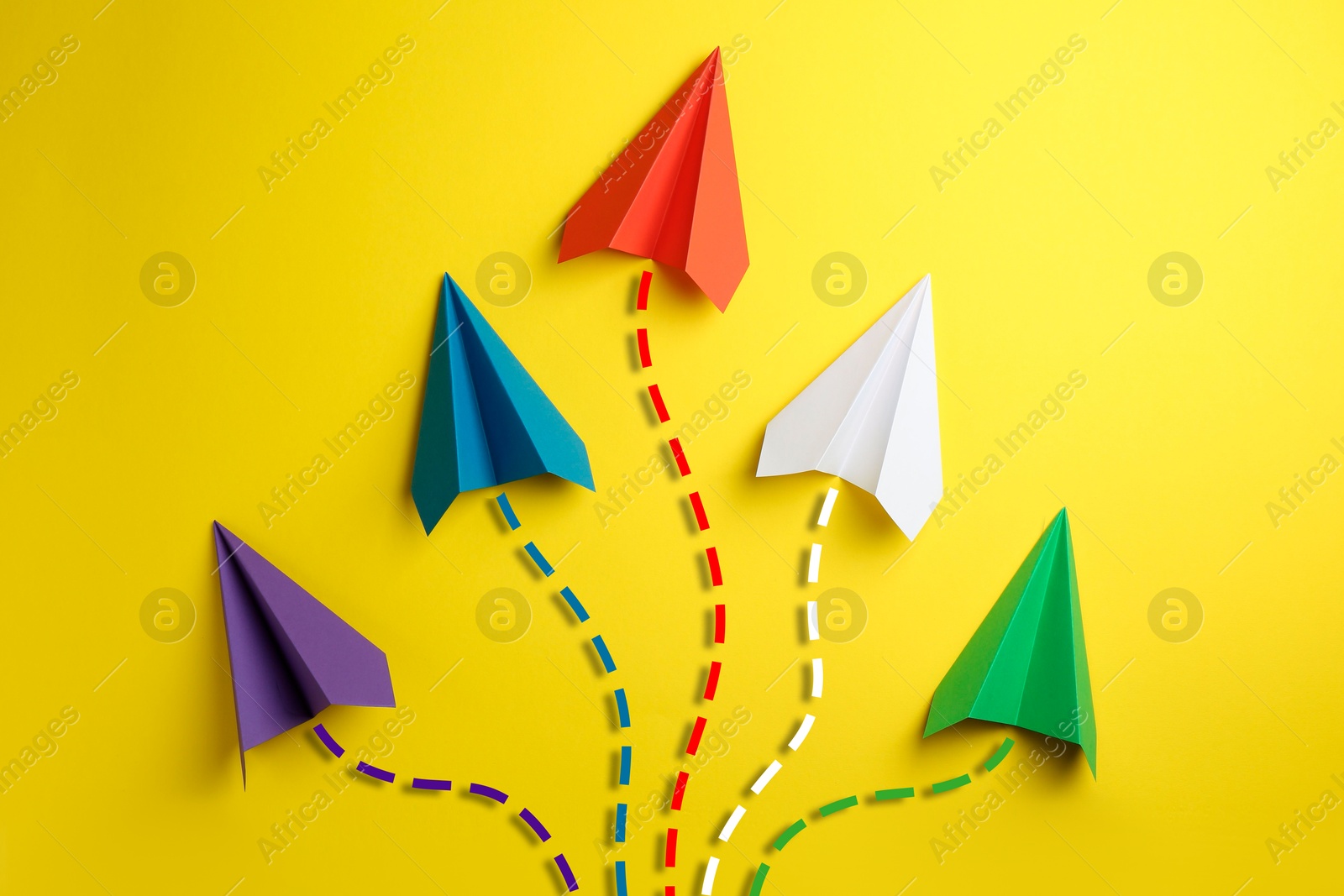 Image of Colorful paper planes with flight paths on yellow background. Dashed lines for trajectory