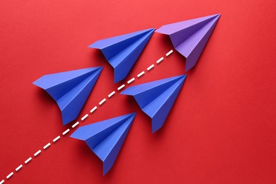 Image of Purple paper plane with flight path among blue ones on red background. Dashed line for trajectory