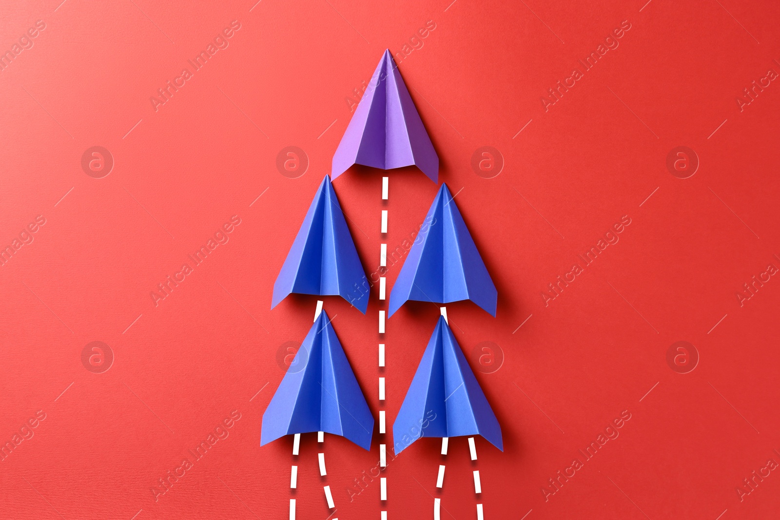 Image of Blue and one purple paper planes with flight paths on red background. Dashed lines for trajectory