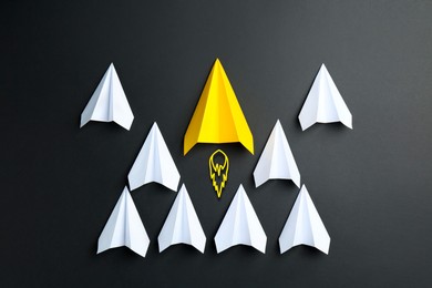 Image of Yellow paper plane bursting forward among white ones on black background