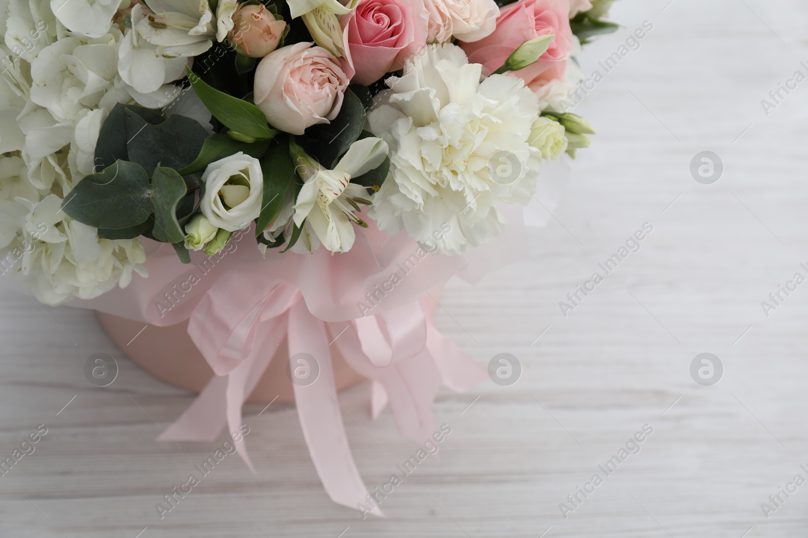 Photo of Beautiful bouquet in box on white wooden table, above view. Space for text