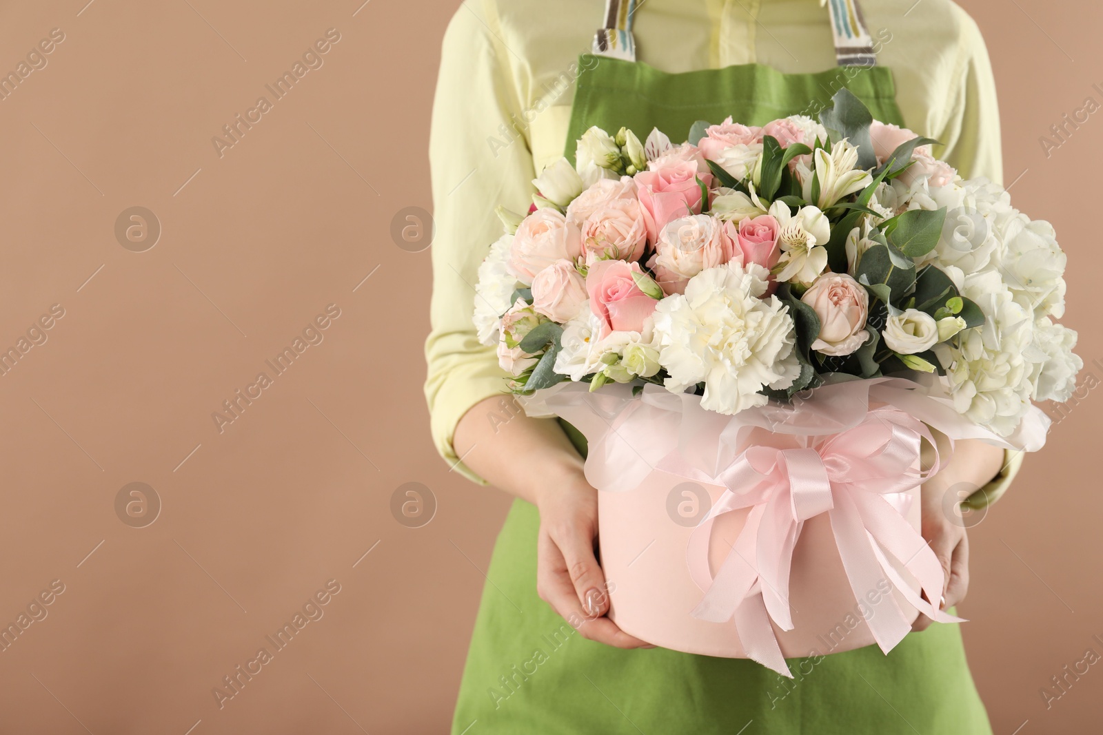 Photo of Florist with beautiful bouquet in box on brown background, closeup. Space for text