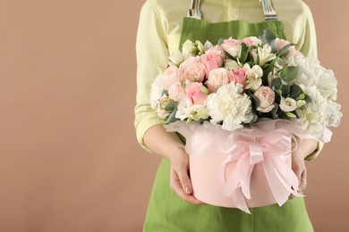 Photo of Florist with beautiful bouquet in box on brown background, closeup. Space for text