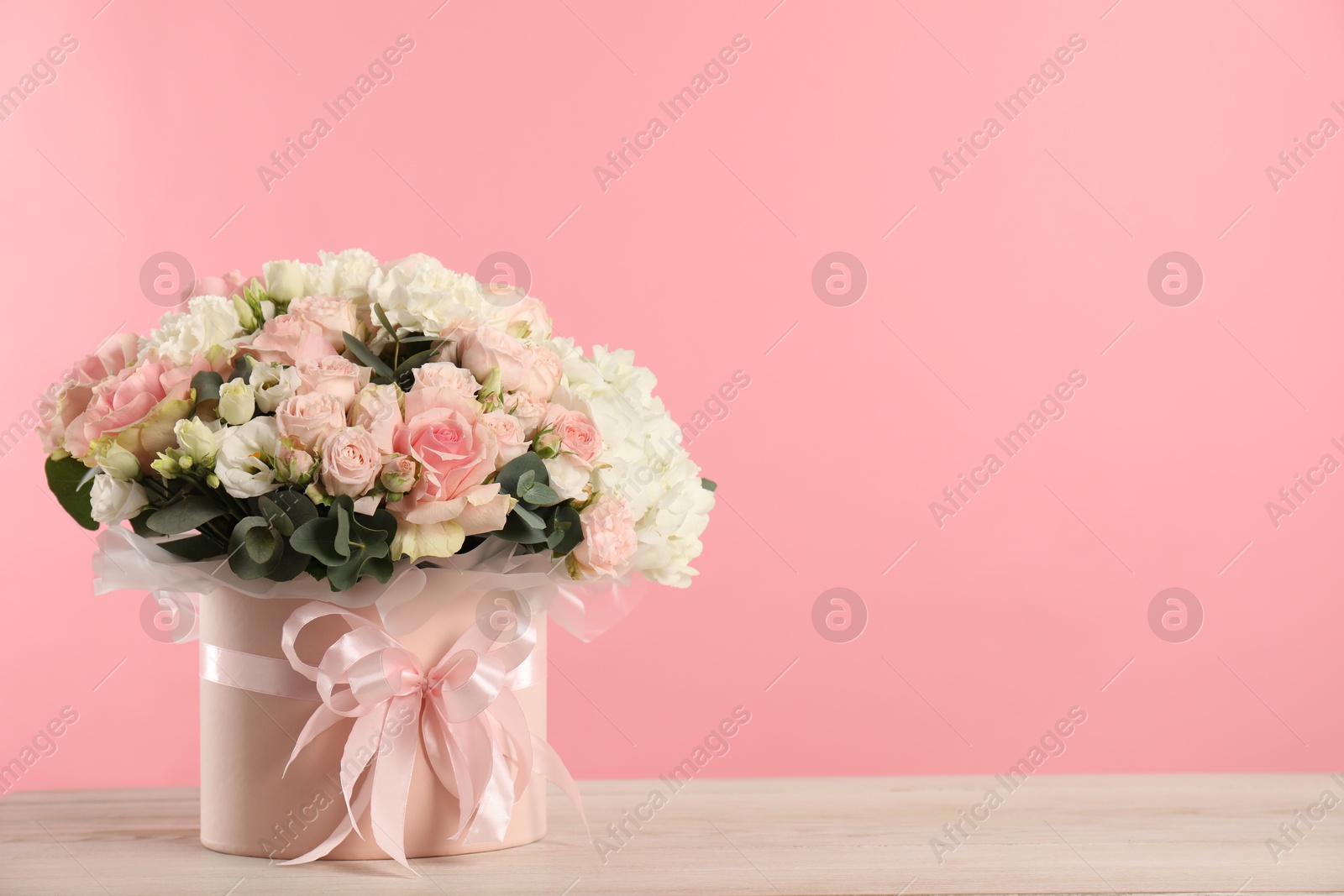 Photo of Beautiful bouquet in box on wooden table against pink background. Space for text