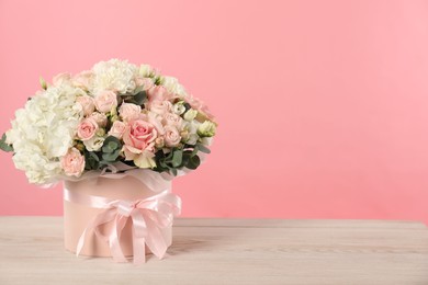 Photo of Beautiful bouquet in box on wooden table against pink background. Space for text