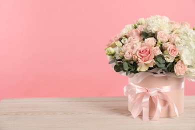 Photo of Beautiful bouquet in box on wooden table against pink background. Space for text