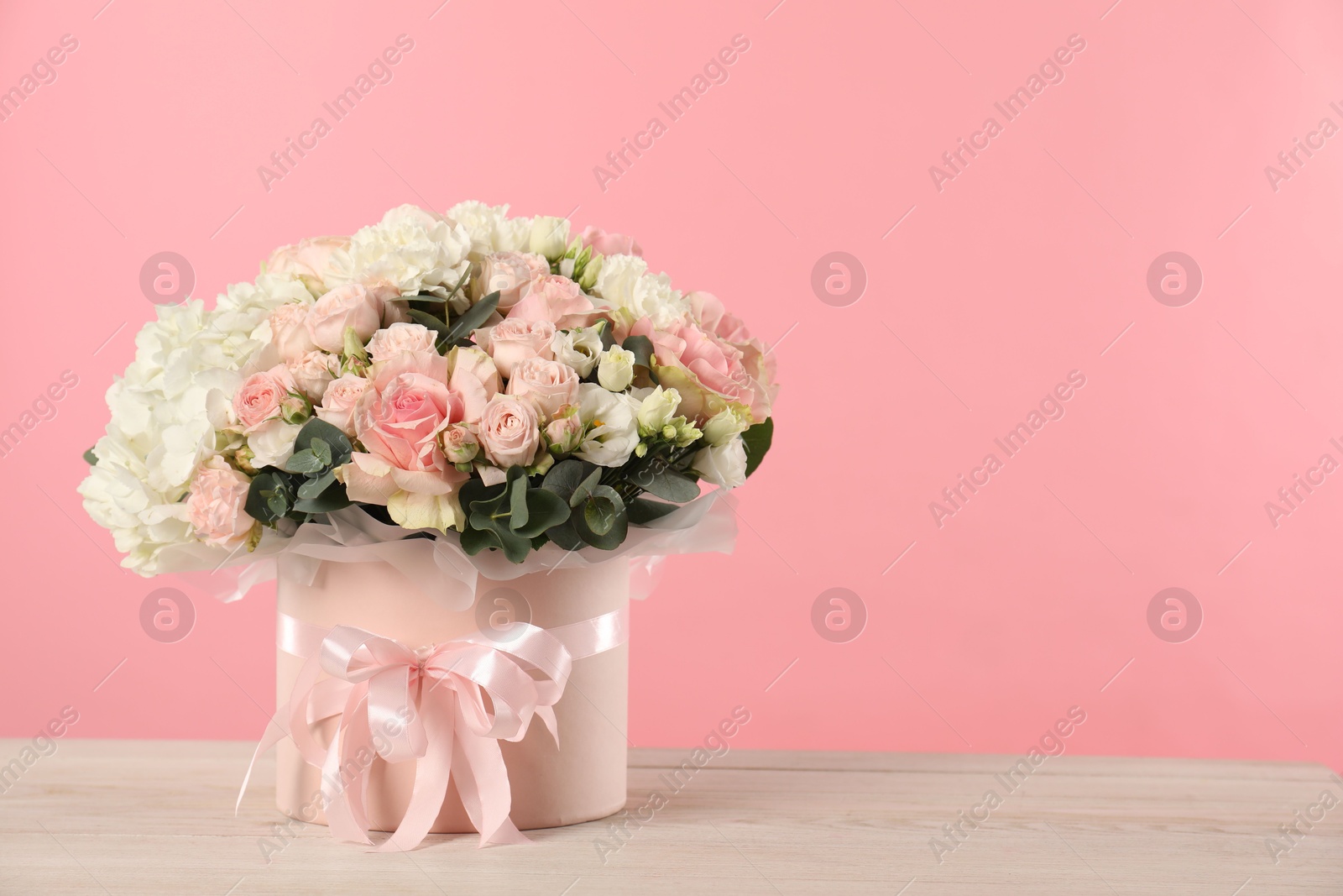 Photo of Beautiful bouquet in box on wooden table against pink background. Space for text