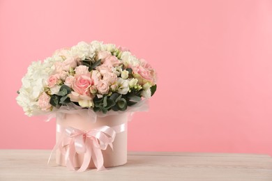 Photo of Beautiful bouquet in box on wooden table against pink background. Space for text