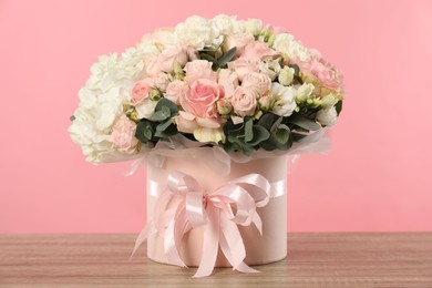 Photo of Beautiful bouquet in box on wooden table against pink background