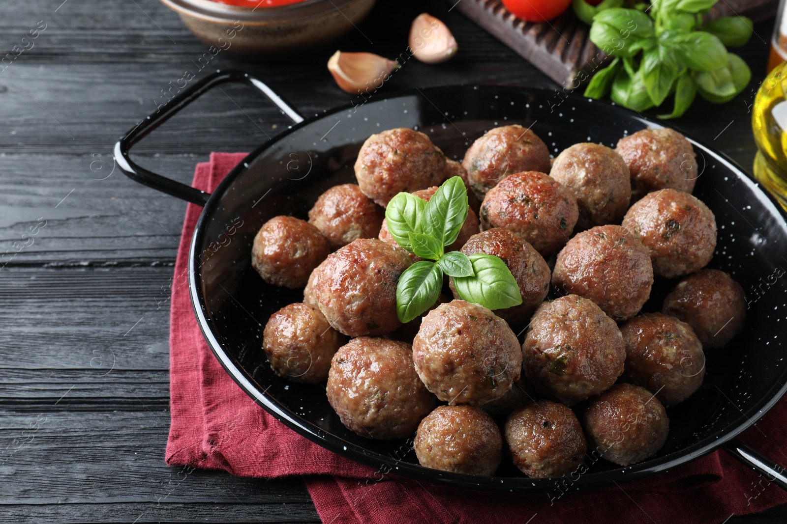 Photo of Tasty cooked meatballs with basil on black wooden table