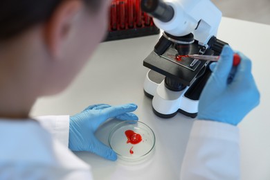 Laboratory testing. Doctor dripping blood sample onto glass slide while working with microscope at table indoors, closeup