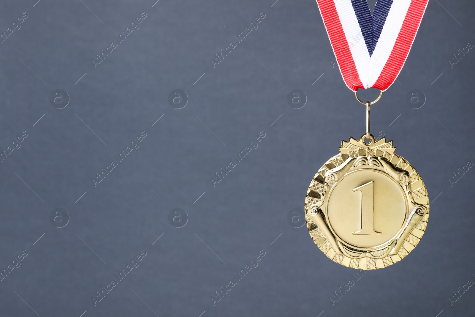 Photo of Golden medal with striped ribbon on grey background, space for text