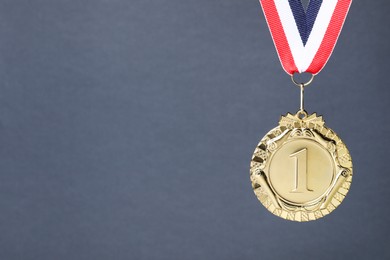 Photo of Golden medal with striped ribbon on grey background, space for text