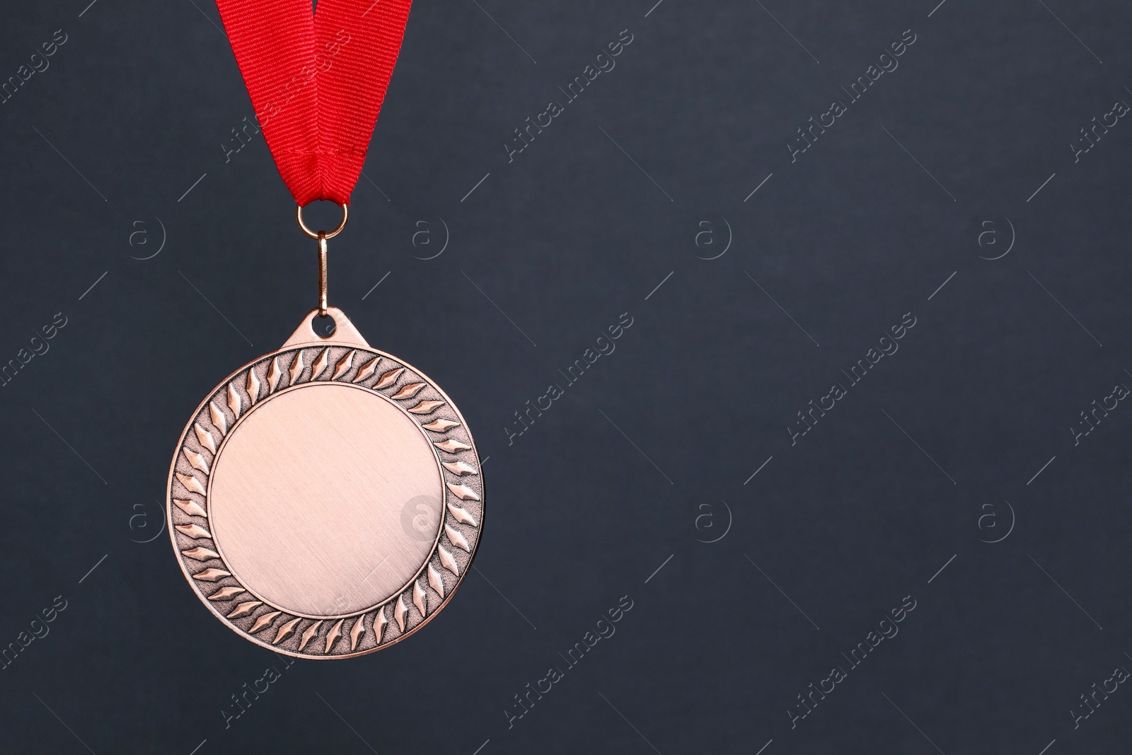 Photo of Bronze medal with red ribbon on dark grey background, space for text