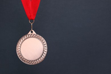 Photo of Bronze medal with red ribbon on dark grey background, space for text