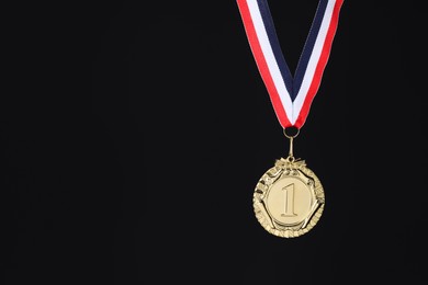 Photo of Golden medal with striped ribbon on black background, space for text