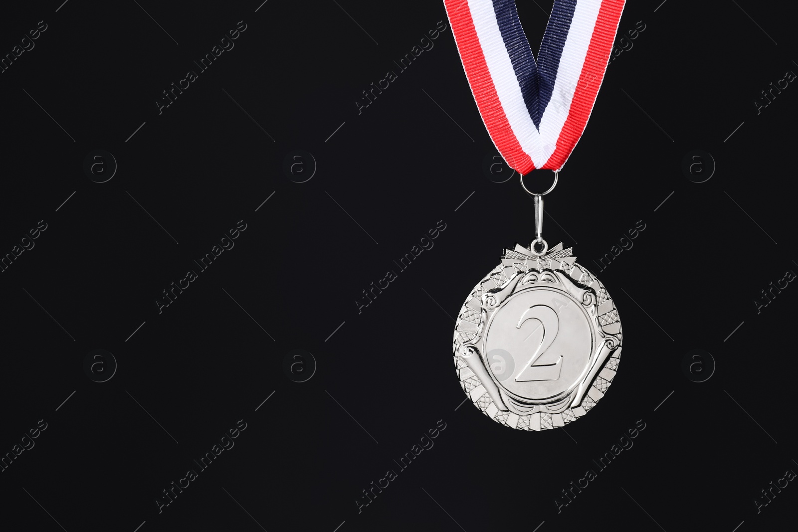 Photo of Silver medal with striped ribbon on black background, space for text