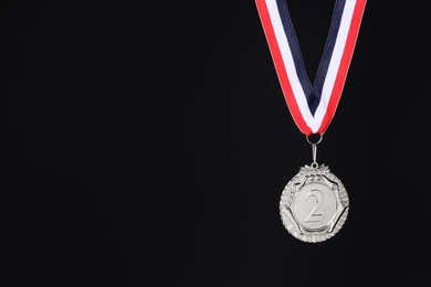 Photo of Silver medal with striped ribbon on black background, space for text