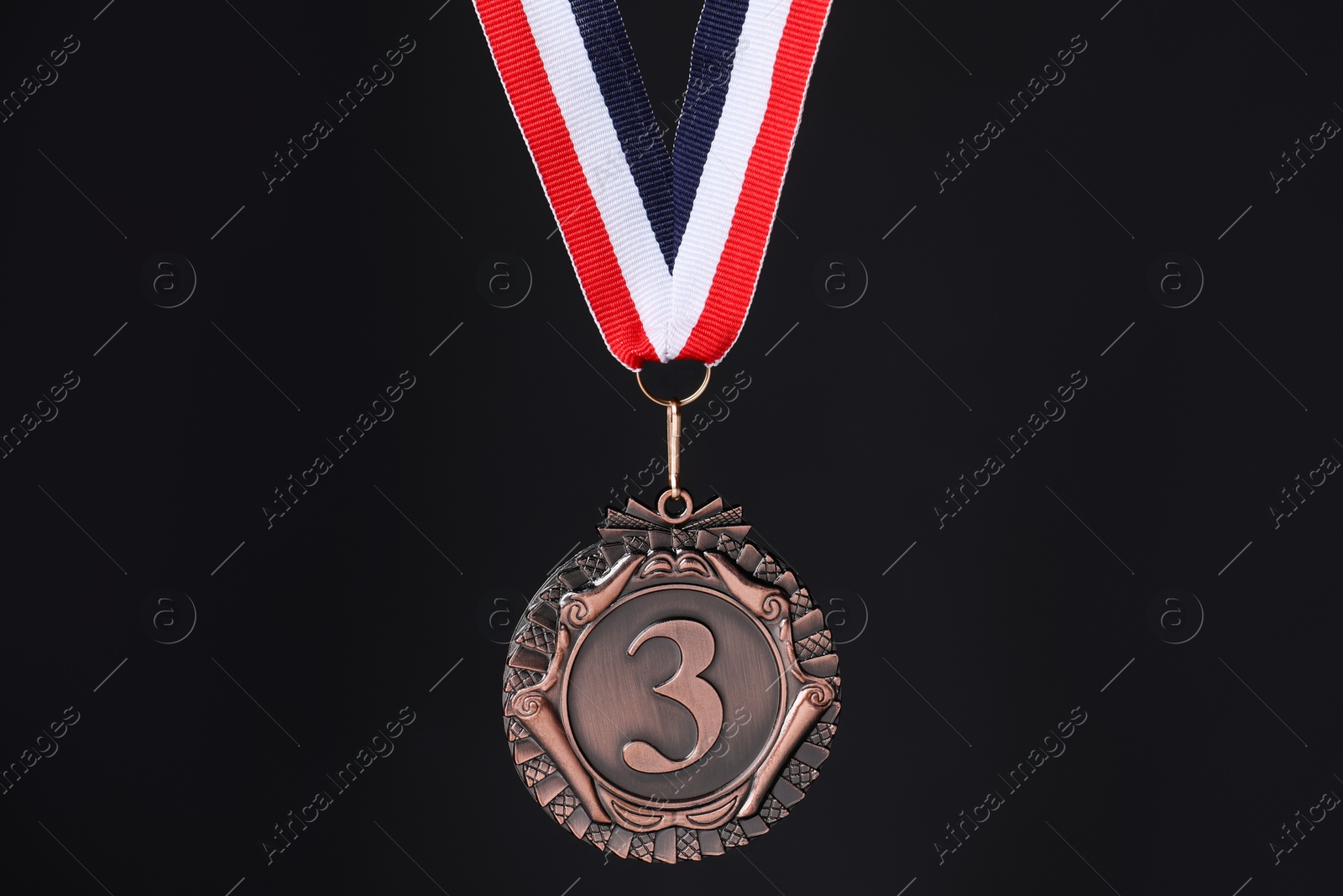 Photo of Bronze medal with striped ribbon on black background