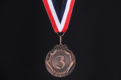 Photo of Bronze medal with striped ribbon on black background