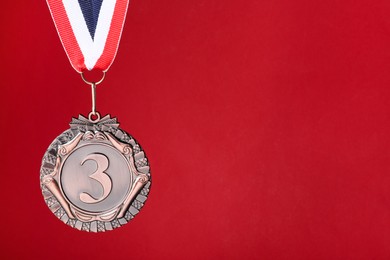 Photo of Bronze medal with striped ribbon on red background, space for text