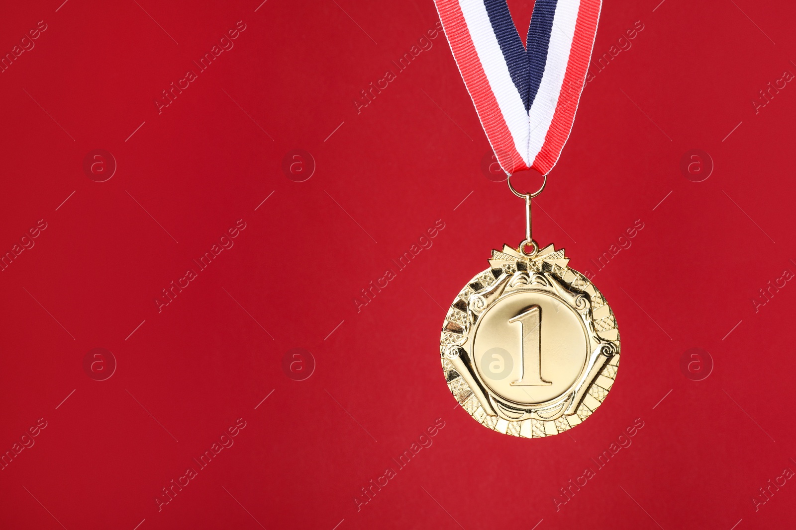 Photo of Golden medal with striped ribbon on red background, space for text