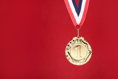 Photo of Golden medal with striped ribbon on red background, space for text