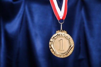 Photo of Golden medal with striped ribbon against blue fabric, space for text