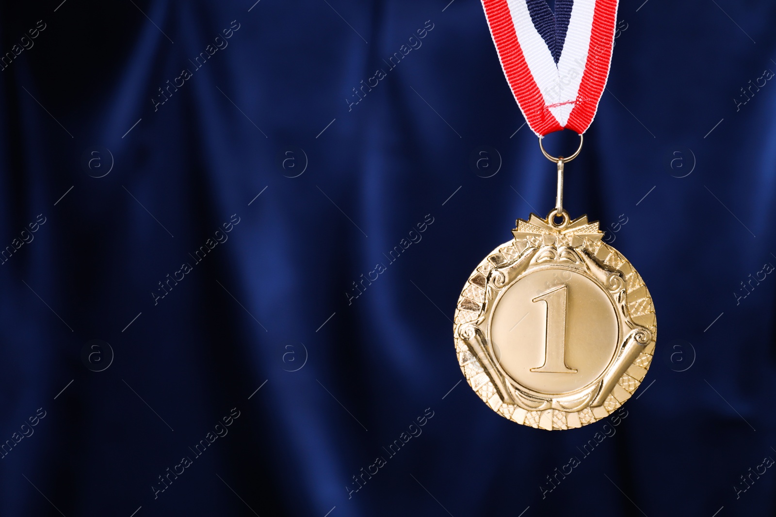 Photo of Golden medal with striped ribbon against blue fabric, space for text