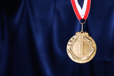 Photo of Golden medal with striped ribbon against blue fabric, space for text