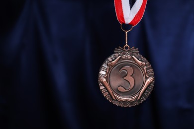 Photo of Bronze medal with striped ribbon against blue fabric, closeup. Space for text