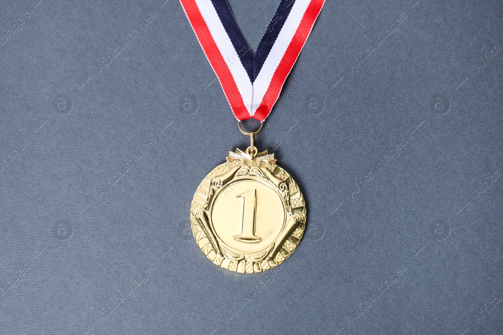 Photo of Golden medal with striped ribbon on grey background, top view