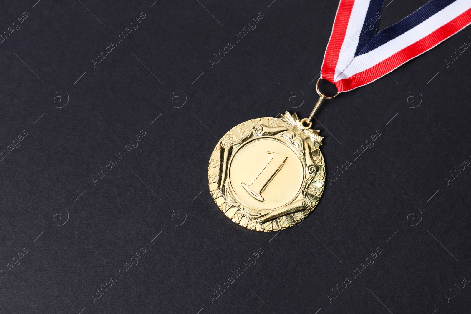 Photo of Golden medal with striped ribbon on black background, top view. Space for text