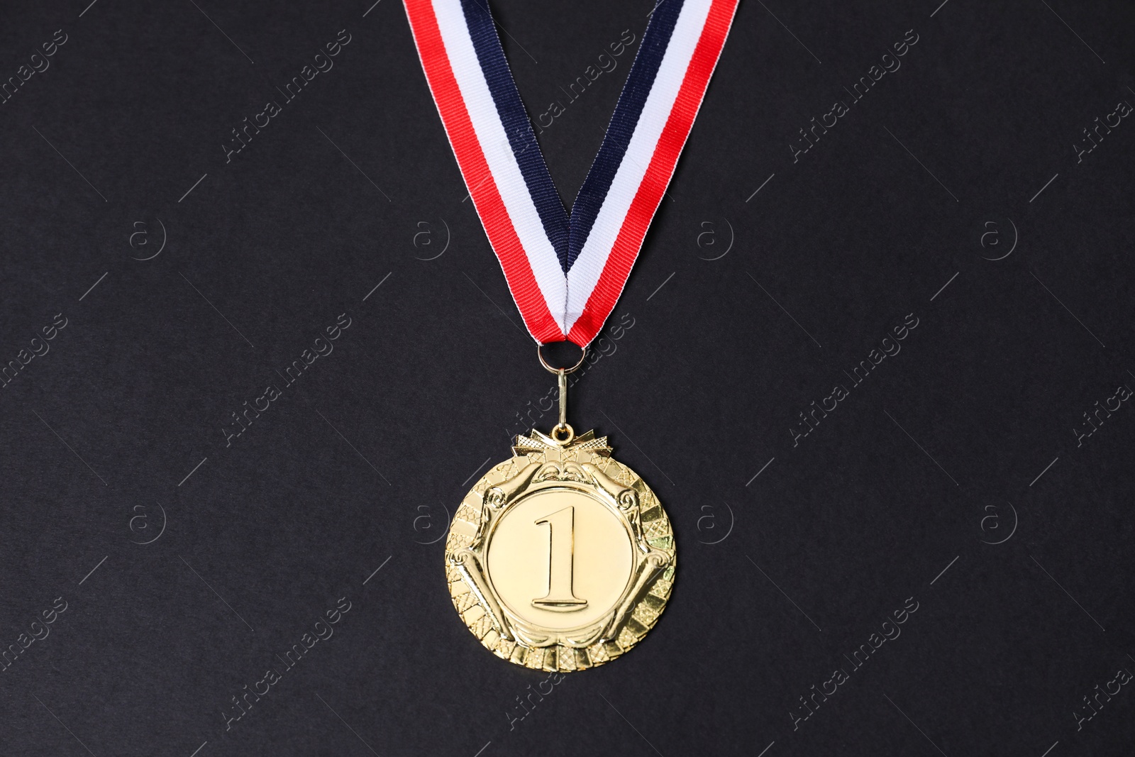 Photo of Golden medal with striped ribbon on black background, top view