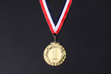 Photo of Golden medal with striped ribbon on black background, top view