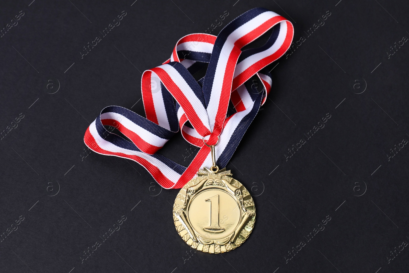 Photo of Golden medal with striped ribbon on black background, top view