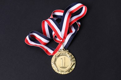 Photo of Golden medal with striped ribbon on black background, top view