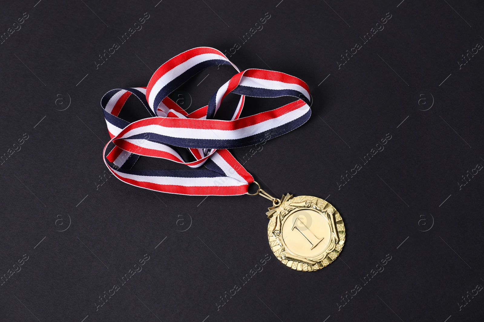 Photo of Golden medal with striped ribbon on black background, above view