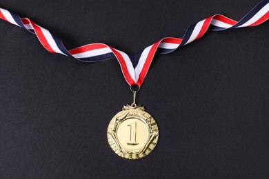 Photo of Golden medal with striped ribbon on black background, top view