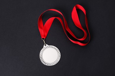 Photo of Silver medal with red ribbon on black background, top view