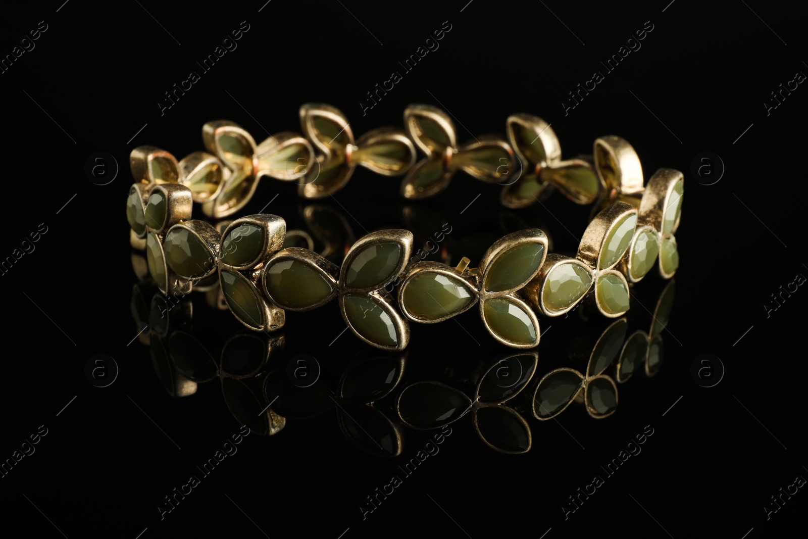 Photo of Beautiful bijouterie. Elegant bracelet on black mirror surface, closeup