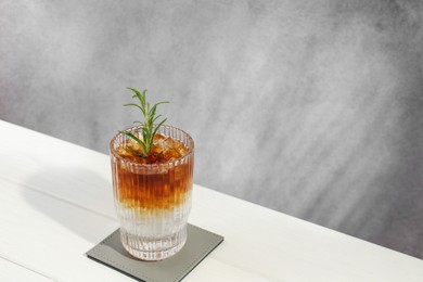 Photo of Refreshing espresso tonic drink with rosemary on white wooden table, space for text