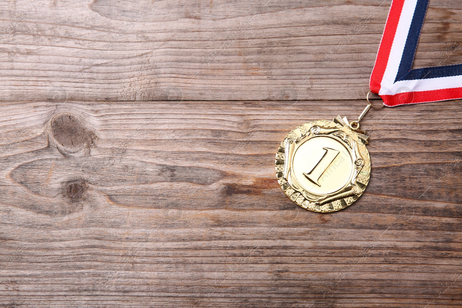 Photo of Golden medal with striped ribbon on wooden background, top view. Space for text