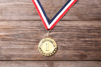 Photo of Golden medal with striped ribbon on wooden background, top view