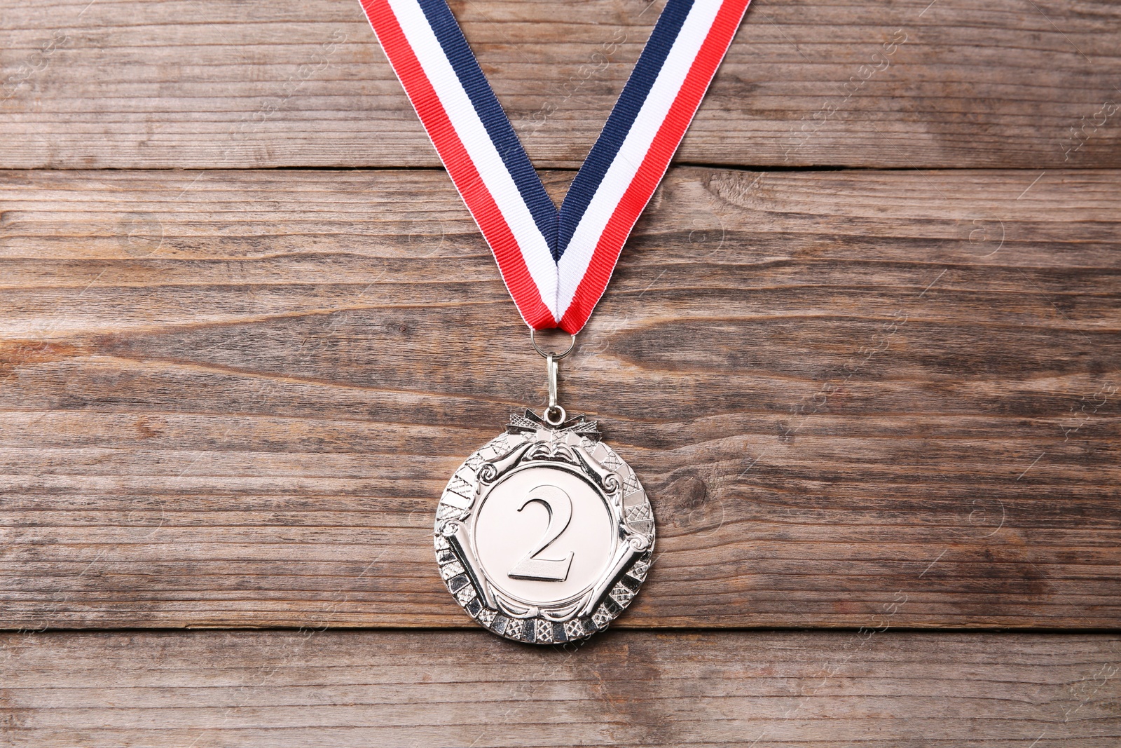 Photo of Silver medal with striped ribbon on wooden background, top view