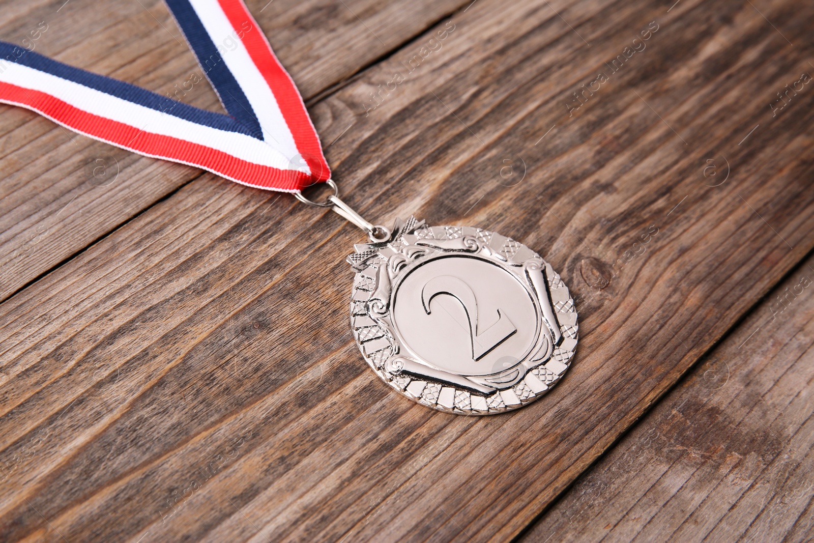 Photo of Silver medal with striped ribbon on wooden background, closeup