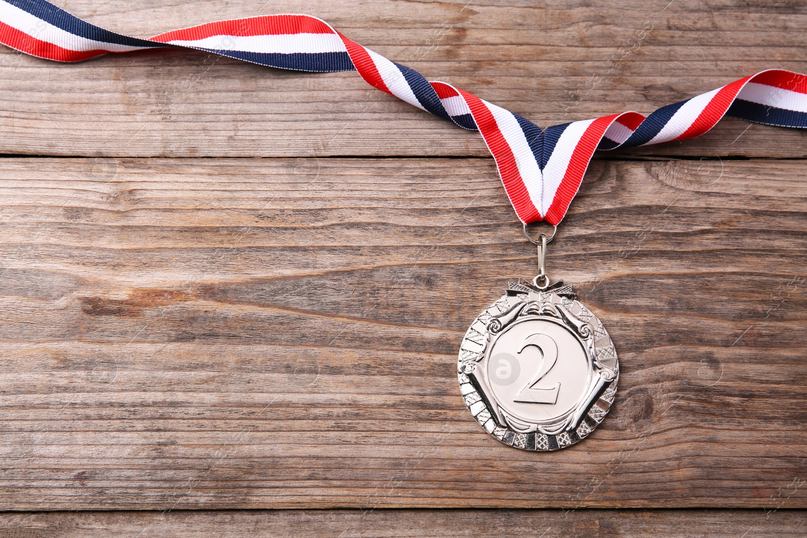 Photo of Silver medal with striped ribbon on wooden background, top view. Space for text