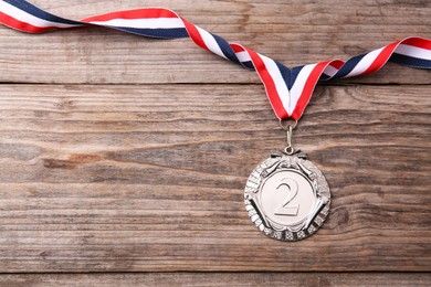 Photo of Silver medal with striped ribbon on wooden background, top view. Space for text