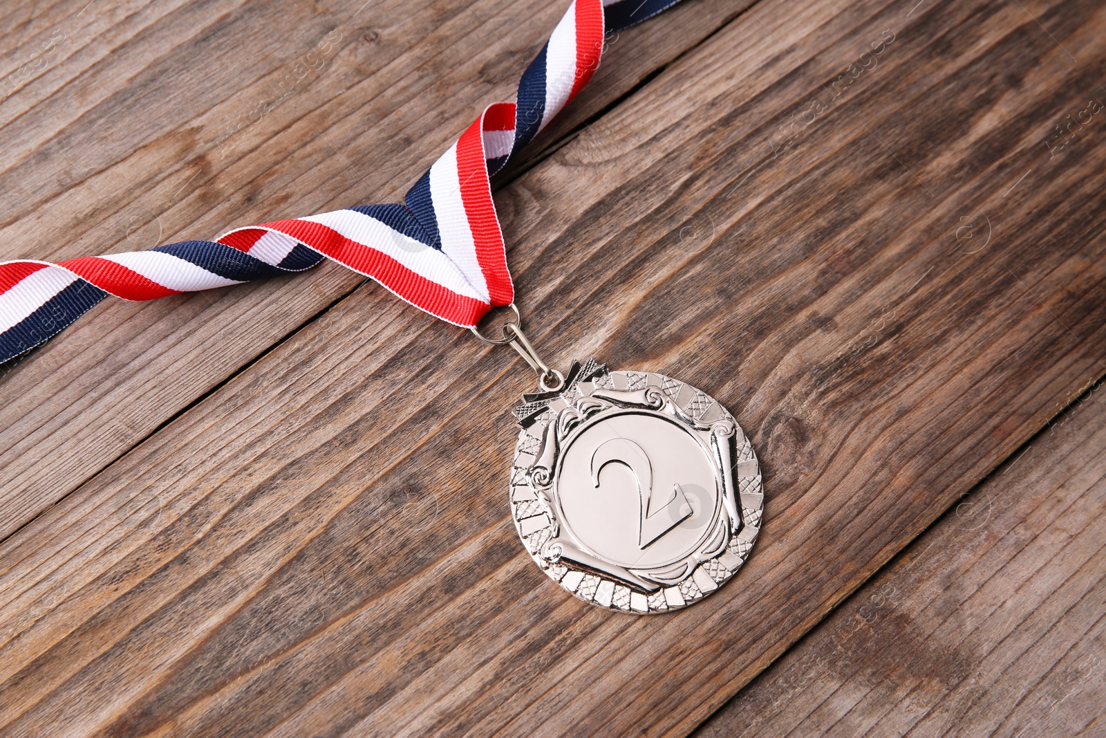 Photo of Silver medal with striped ribbon on wooden background, above view